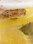 Close-up view of a carbonated yellow liquid with bubbles forming along the surface and within the liquid. The frothy foam on top suggests it is a beverage, possibly beer or a soft drink.