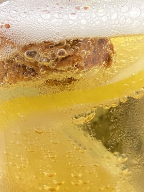 Close-up view of a carbonated yellow liquid with bubbles forming along the surface and within the liquid. The frothy foam on top suggests it is a beverage, possibly beer or a soft drink.