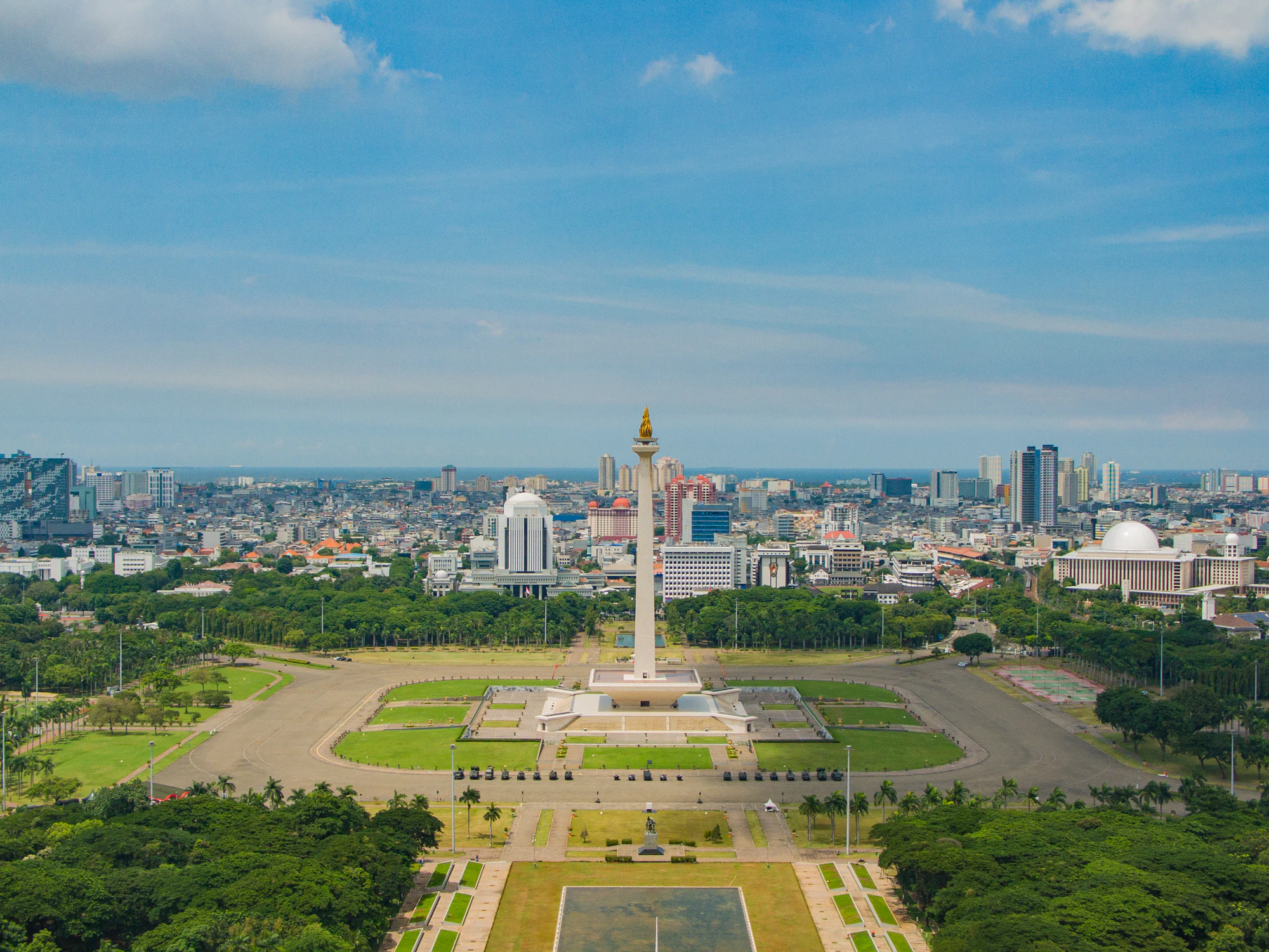 The National Monument standing at the centre of Merdeka Square in Jakarta, seen from the air with the city skyline spread out behind it