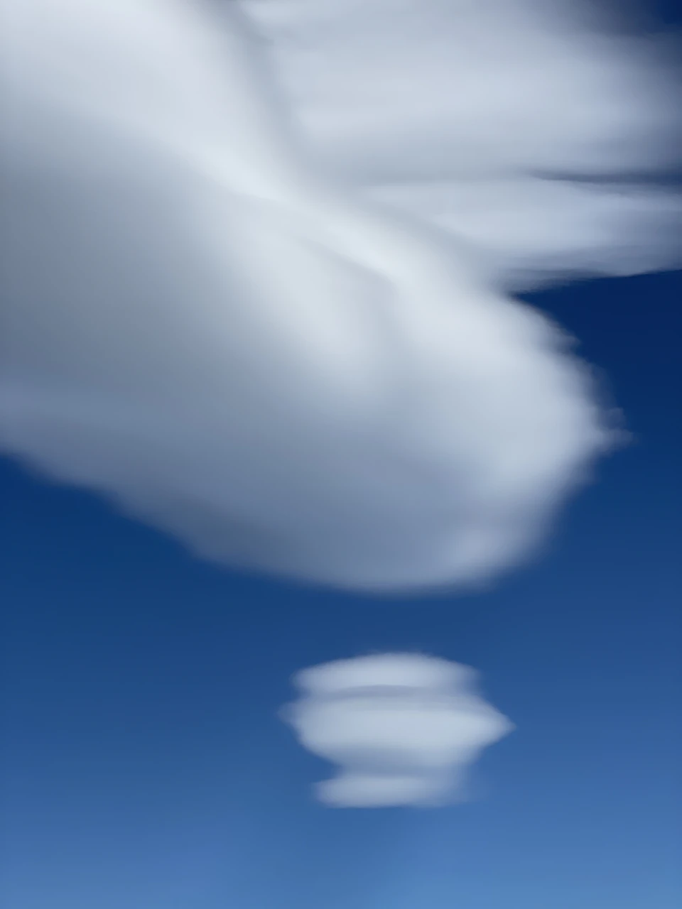 Two clouds float in the sky, one large and white, one small and rounded
