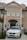 A white BMW car is parked in front of a building with beige walls and multiple windows, featuring arched designs. The building has a sign at the top with the word 'BONONIA'. There is a black lamp post on the left, and some green shrubs surrounding the area.