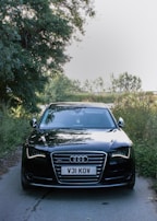 An Audi A8 gliding smoothly on a tree-lined avenue with the sun reflecting off its glossy black finish.