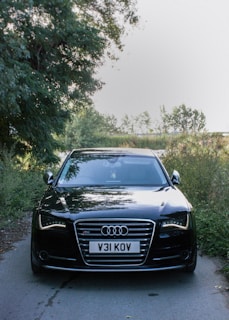 An Audi A8 gliding smoothly on a tree-lined avenue with the sun reflecting off its glossy black finish.