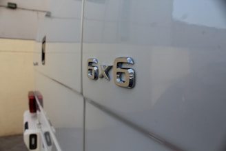 A close-up view of a vehicle's side, featuring a chrome '6x6' badge that indicates the vehicle has six-wheel drive. The background includes a part of the truck bed and a wall.
