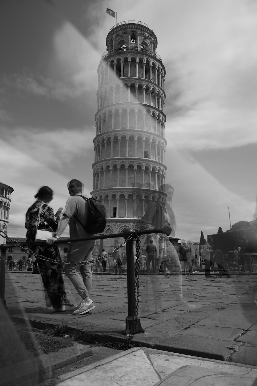 um homem e uma mulher andando em frente a uma grande torre com a Torre Inclinada de Pisa no fundo