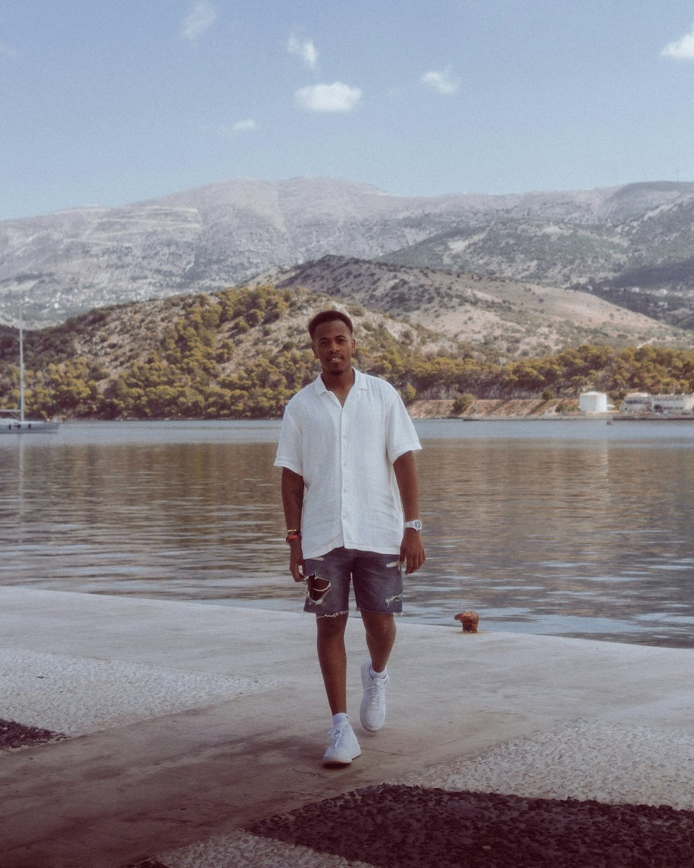 a man standing by a body of water with mountains in the background