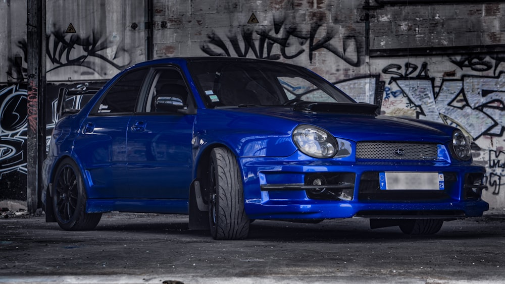 a blue car parked in front of a wall with graffiti