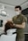 A dentist is attending to a patient in a dental clinic. The dentist is wearing a face mask and gloves, focusing on the task. The patient is seated in a dental chair with an overhead light, and there is a serene atmosphere.