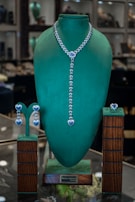 A jewelry display in a store showcases a set of jewelry with blue gemstone accents. The centerpiece is an elegant necklace with a heart-shaped design and matching earrings. The pieces are presented on a green velvet display stand, giving a luxurious and sophisticated appearance.