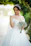 Bride smiling happily wearing a delicate floral hairpiece during a sunny outdoor ceremony.