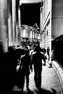 Black and white photograph of a bustling 1920s city street at dusk, capturing fleeting expressions of passersby.