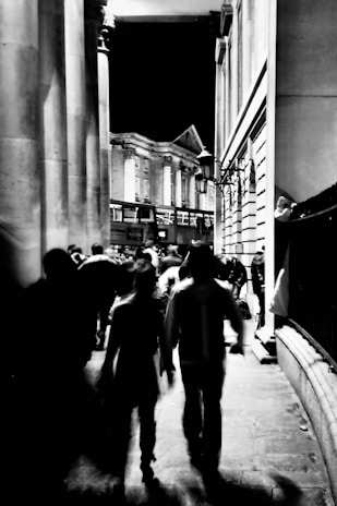 Black and white photograph of a bustling 1920s city street at dusk, capturing fleeting expressions of passersby.