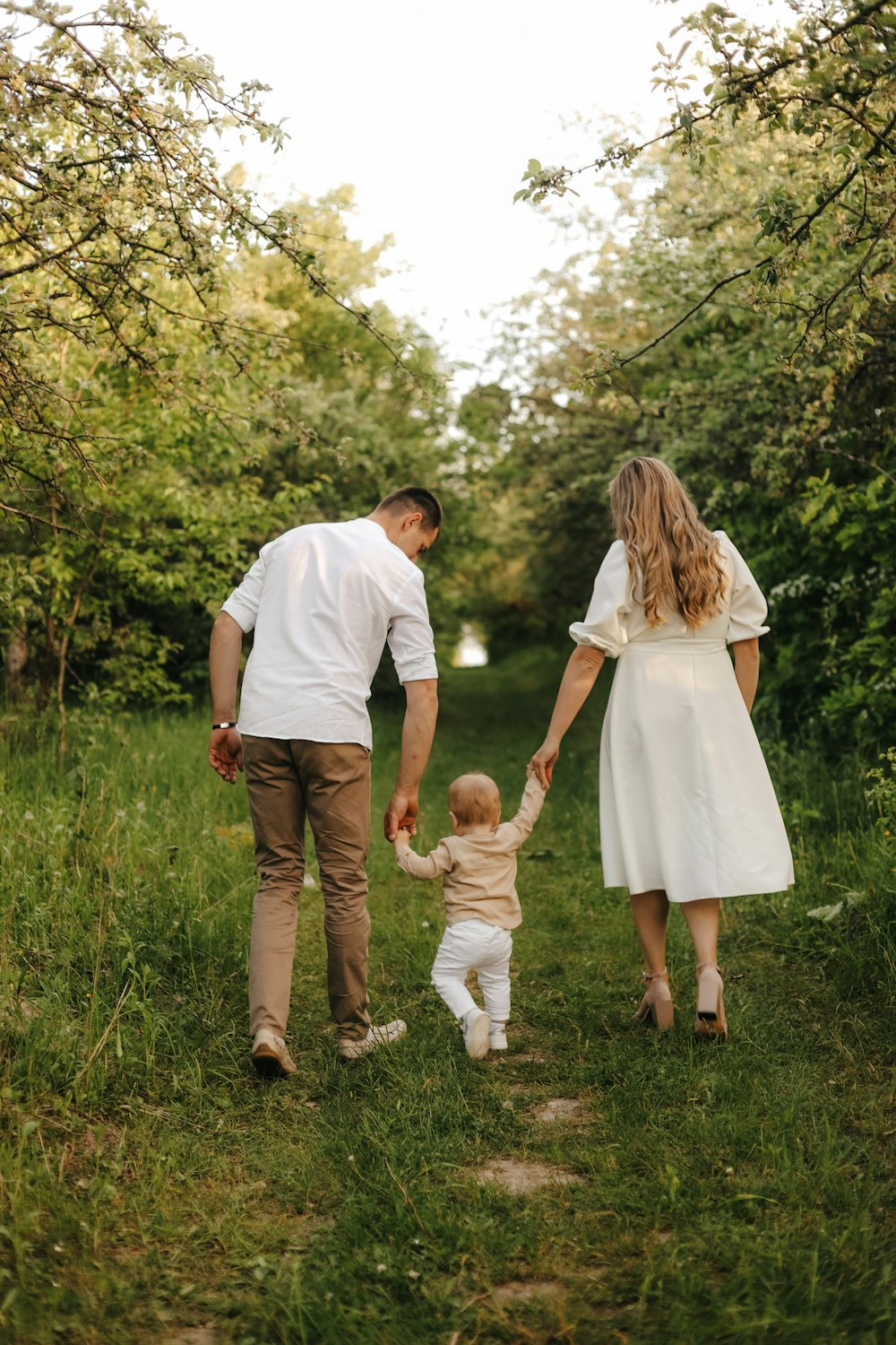 a man and woman holding hands with a baby in a grassy area