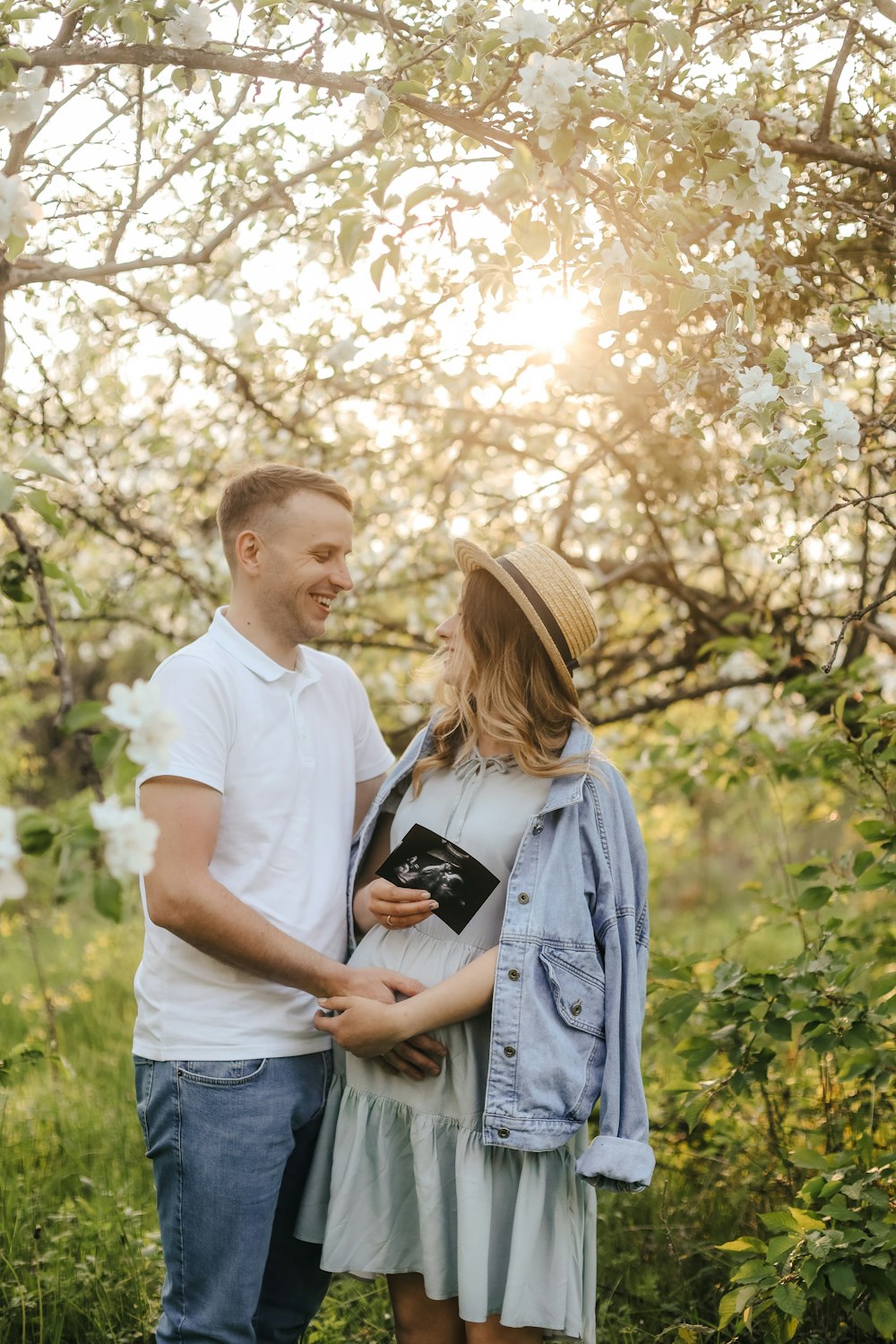 a man and woman standing in a field with trees and flowers