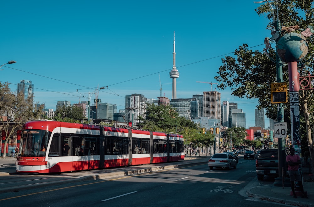 a red and white trolley on a street with cars and buildings in the background