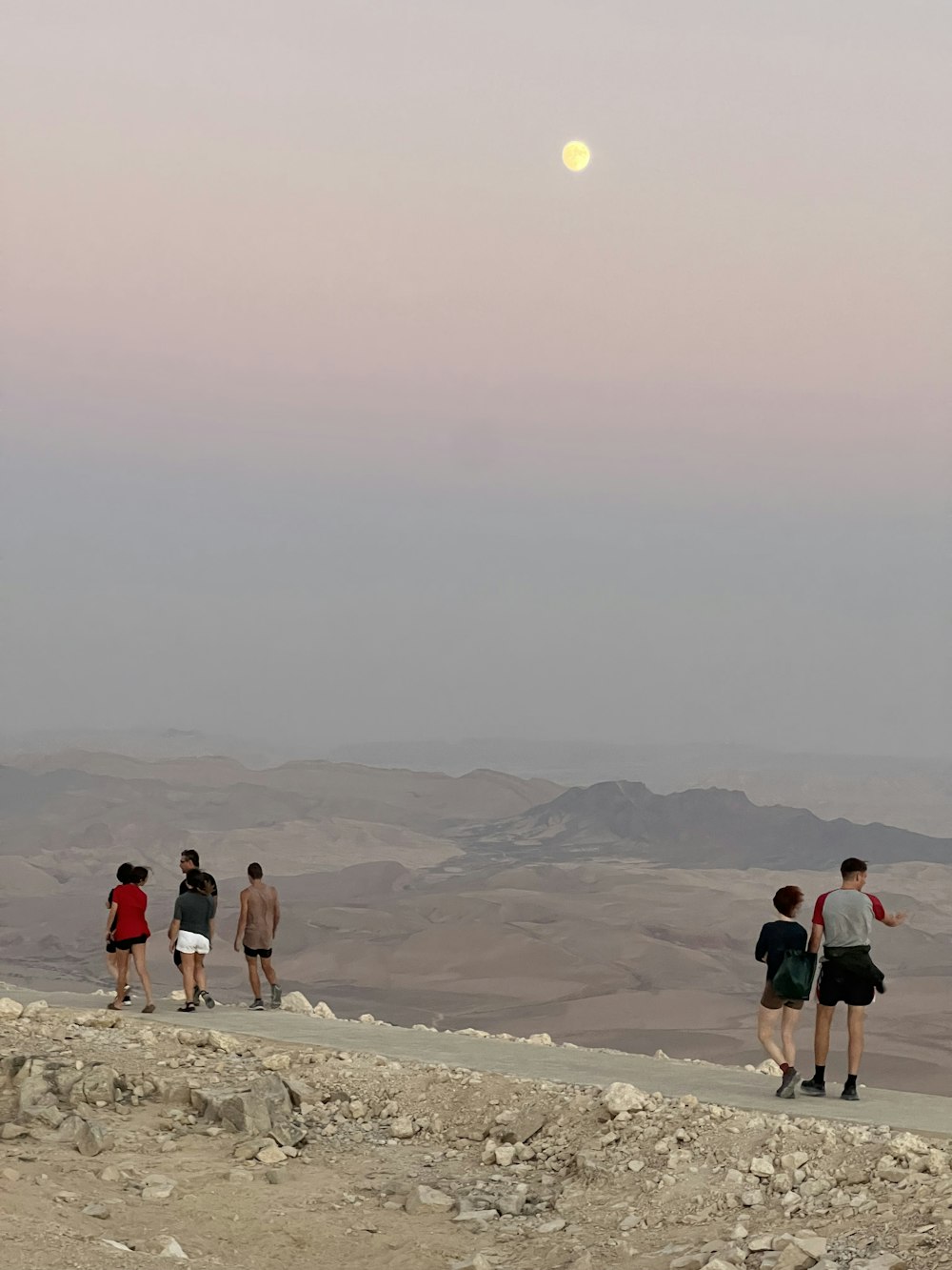 Un grupo de personas caminando sobre una colina rocosa con una luna en el cielo