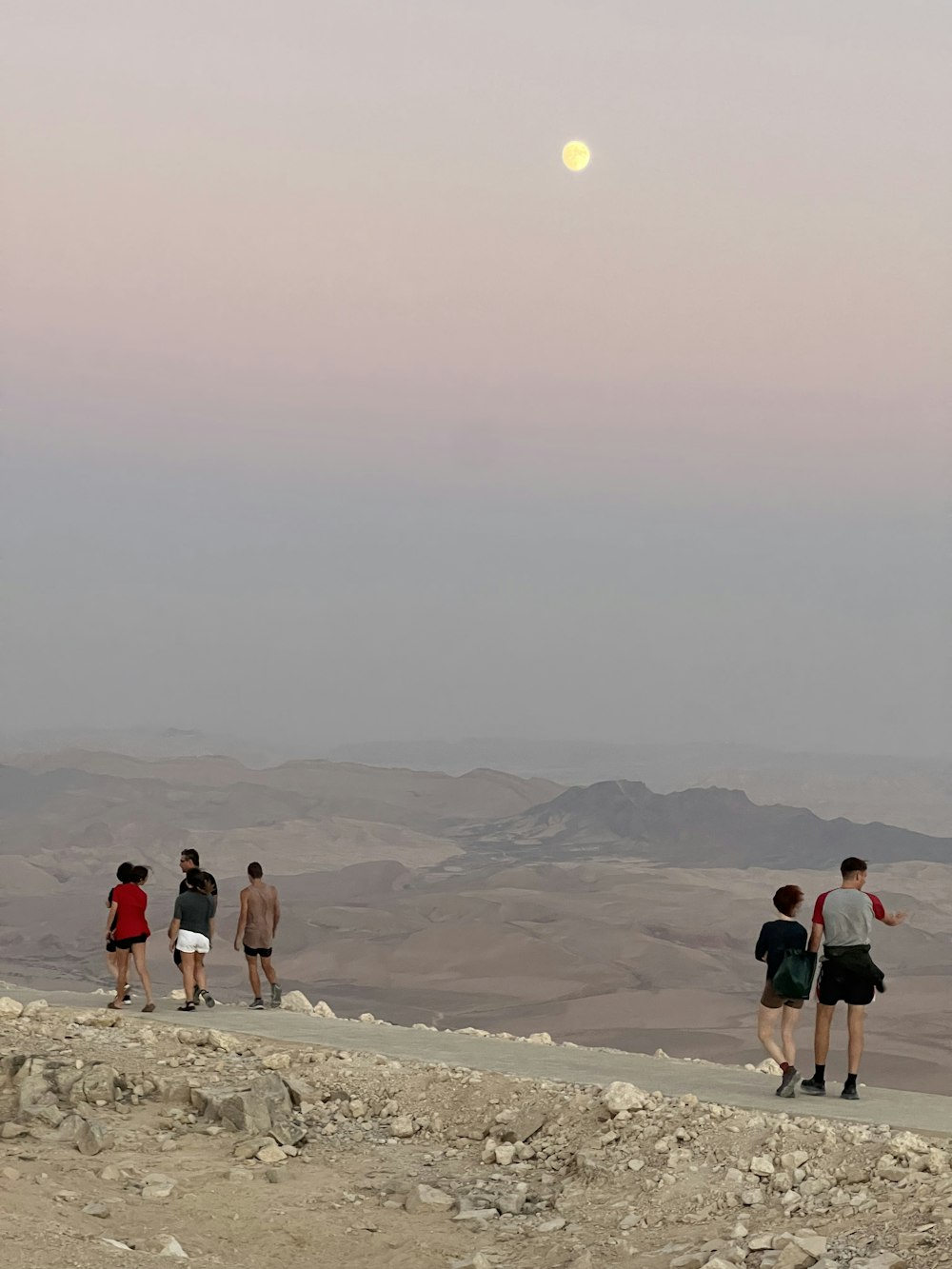 a group of people walking on a rocky hill with a moon in the sky