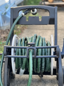 A garden hose coiled onto a portable hose reel with a handle, placed on a concrete surface. The hose is green with a textured pattern and the reel has a black frame with white sides.
