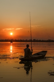 a person sitting in a boat on a lake at sunset