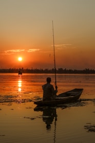 a person sitting in a boat on a lake at sunset