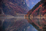 A serene lake reflecting the dramatic cliffs and vibrant autumn foliage in West China.