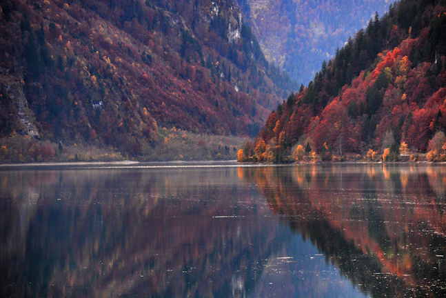 A serene lake reflecting the dramatic cliffs and vibrant autumn foliage in West China.