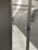 A corridor inside a data center with rows of server racks enclosed within glass panels. Overhead lighting brightly illuminates the area, and perforated floors suggest climate control measures.
