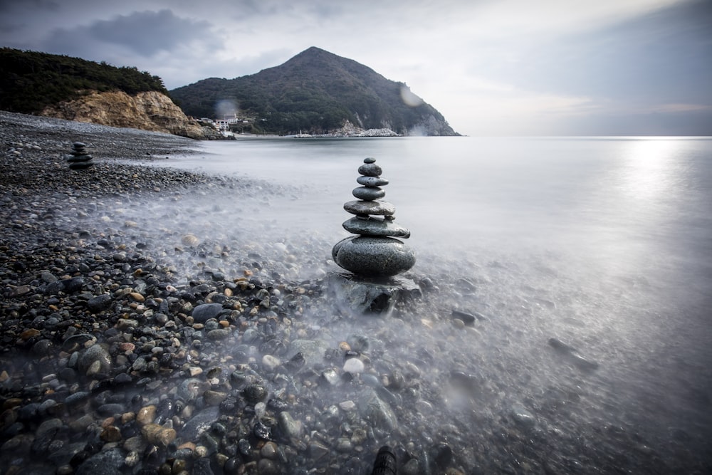 a rocky beach with a large stack of rocks in the water
