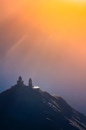 A serene sunrise over a peaceful church with worshippers raising their hands in praise.