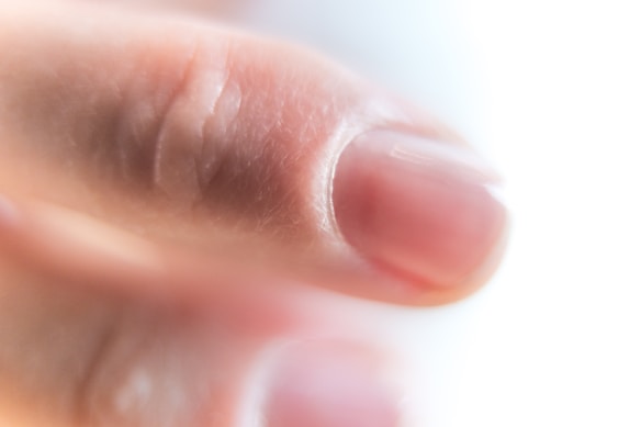 A close-up view of a human finger, focusing on the nail and surrounding skin. The image emphasizes the texture and details of the skin, showing natural skin tones.
