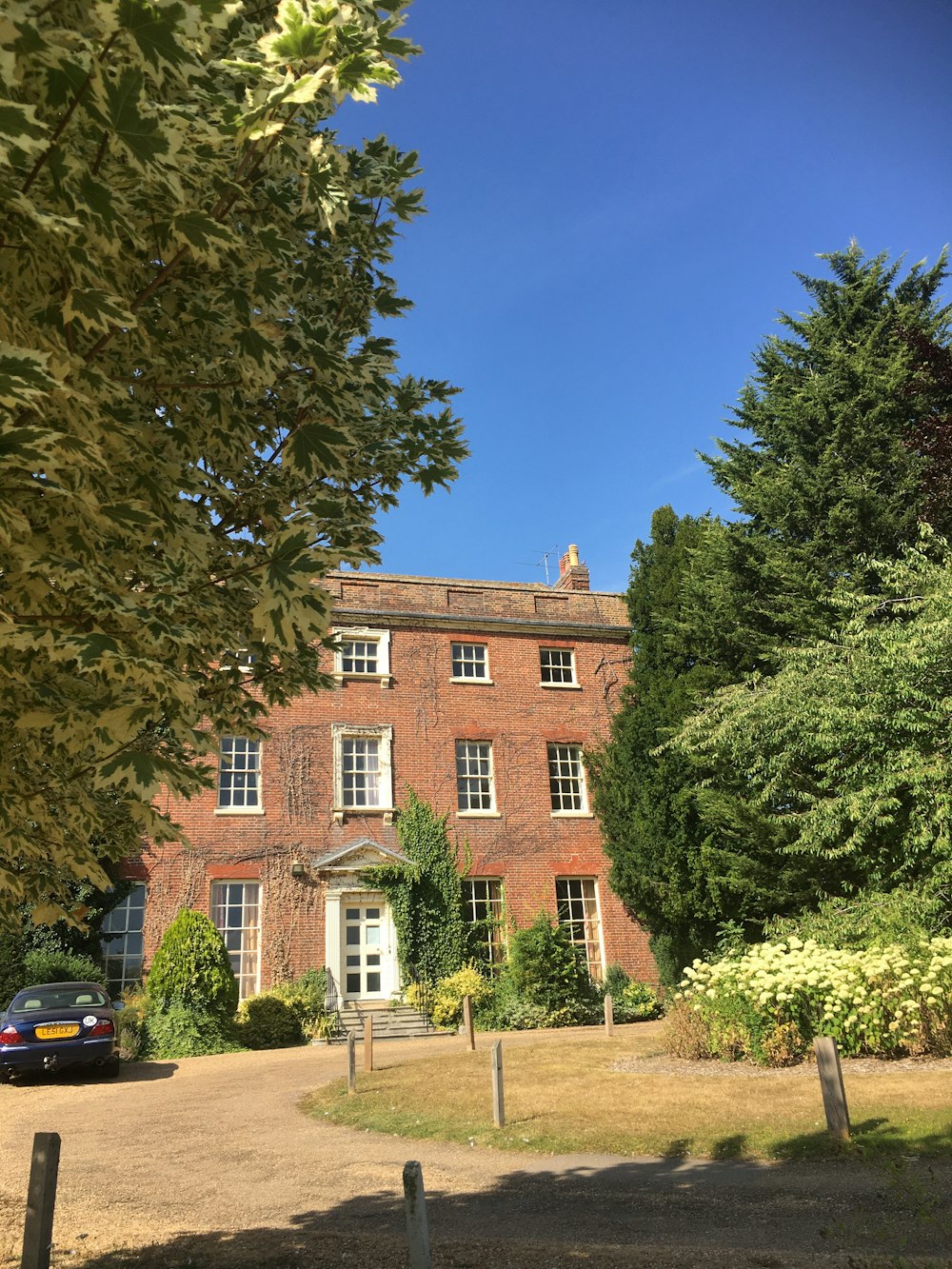 a brick building with trees and a blue car parked in front