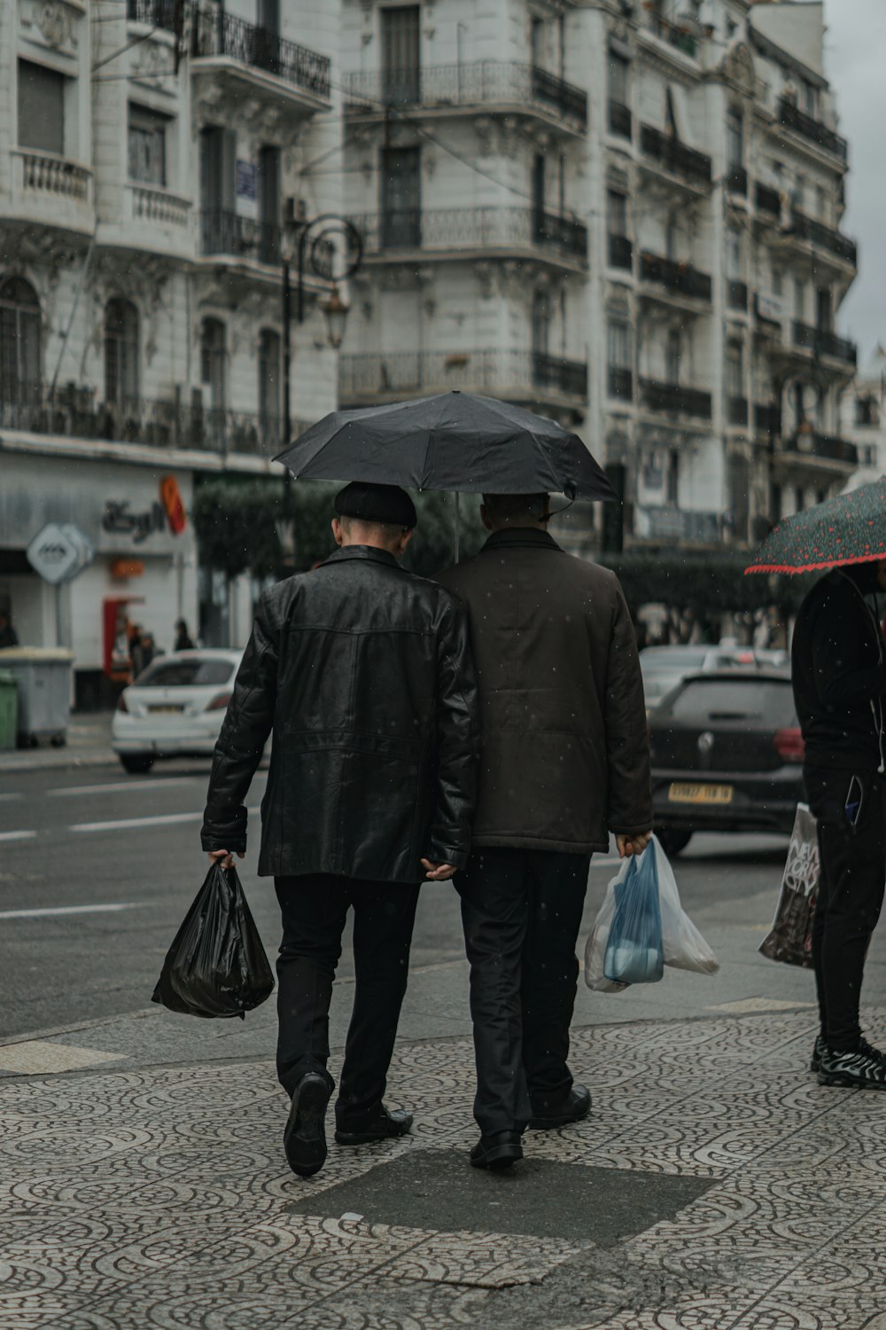 a couple of men walking down a sidewalk with an umbrella