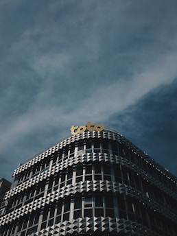 A modern building with a unique façade featuring geometric patterns and a yellow sign on top displaying the word 'toto'. The sky is cloudy, casting a slightly moody atmosphere over the scene.