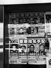 A poster displaying several headshots of individuals accompanied by text, likely in Japanese. The poster is monochrome, featuring both men and a woman, with names and other details printed next to each photo. The photos appear to be mugshots or identification photos.