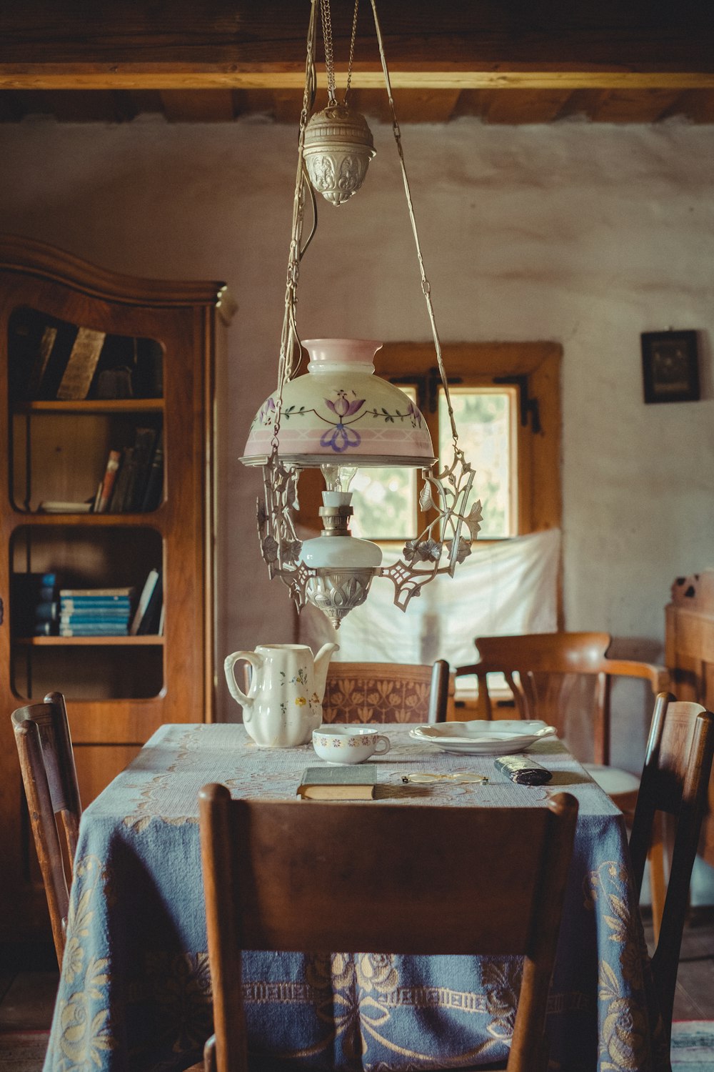 a dining table with a lamp and a shelf with books