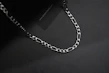 Close-up shot of a stylish silver chain resting on a minimalist black surface, highlighting fine craftsmanship.
