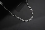 Close-up shot of a stylish silver chain resting on a minimalist black surface, highlighting fine craftsmanship.