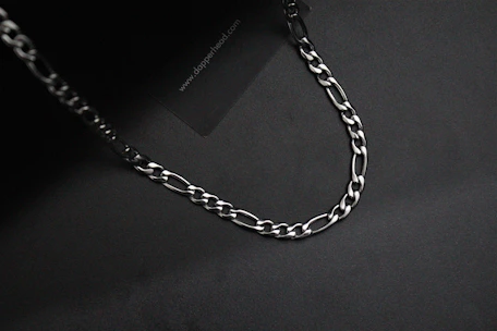 Dark background with a spotlight on a collection of sleek black collars and chains arranged artistically.