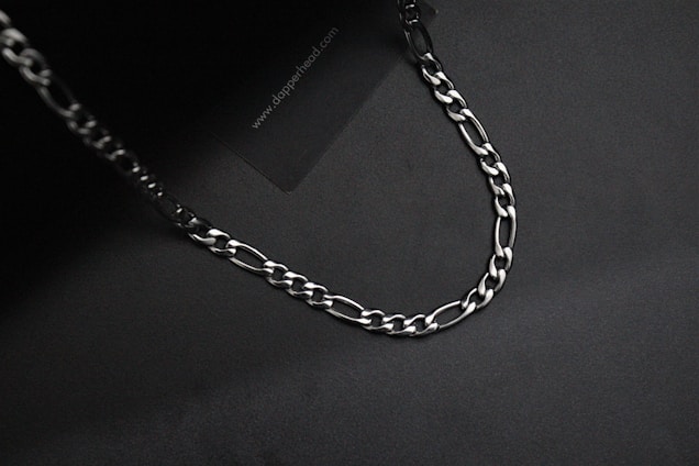 Close-up of a sleek black and gold rapper-style chain glistening under soft lighting on a dark background.