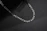 Close-up of a sleek silver men's chain resting on dark marble background.