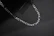 Man wearing sleek silver chain and matching ring on dark marble background.