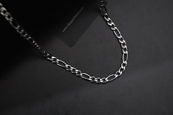 A silver chain with interlocking links is laid out on a dark, almost black background. The lighting creates subtle reflections on the metal surface.