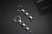 Two metallic chain earrings with square links are placed on a dark surface. Alongside is a partial view of a business card with text.