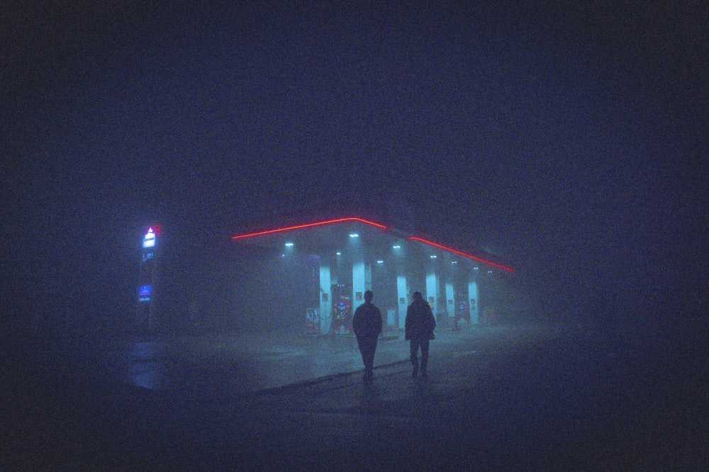 a couple of people walking in front of a building with lights