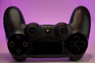 A black gaming controller placed against a soft purple background, highlighting its sleek design with various buttons and joysticks.