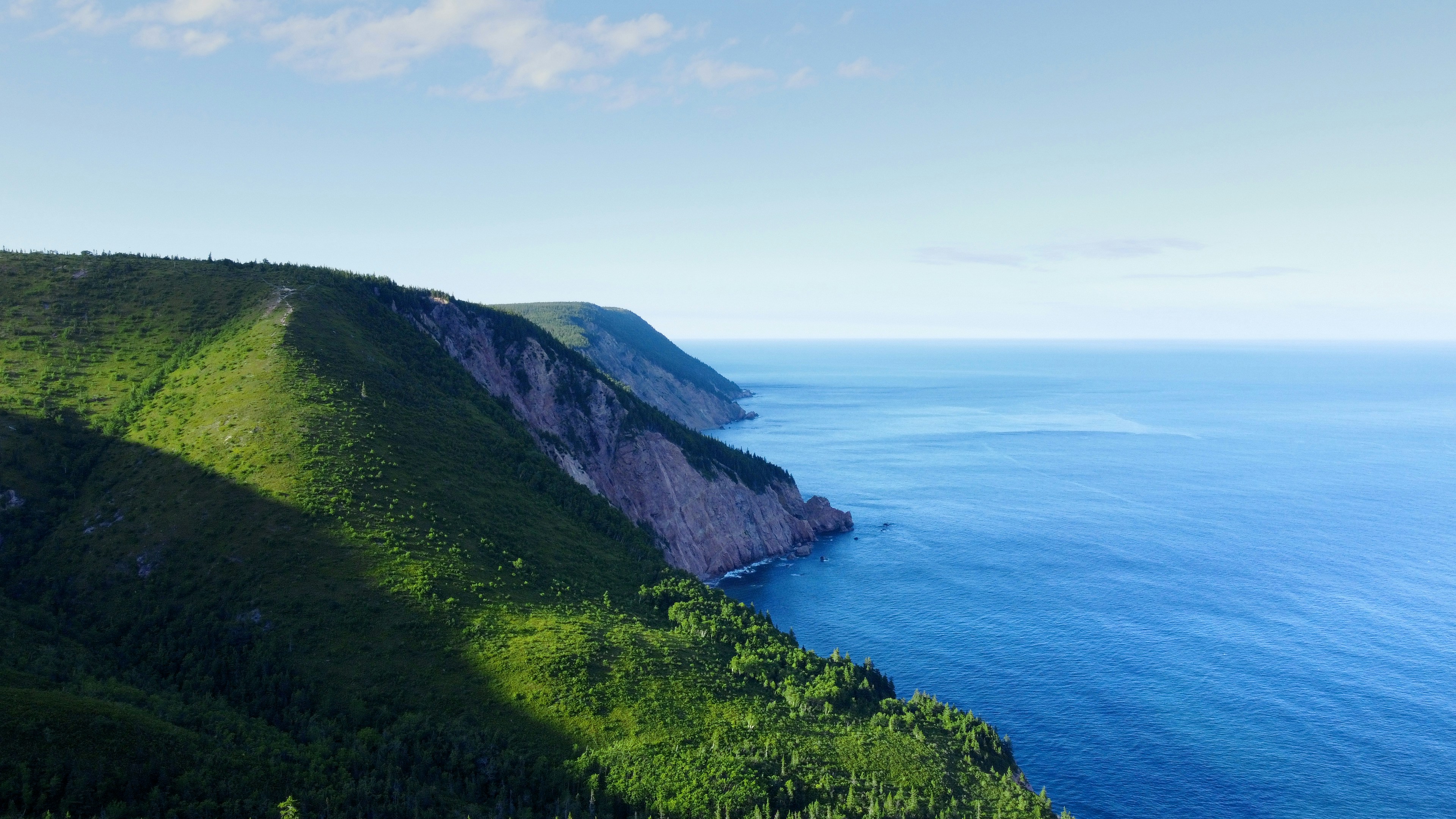 a cliff next to a body of water, Drone shot of mountains next to the ocean on the Cabot Trail