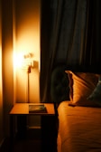 A warm-toned bedroom corner with layered textiles and a small reading lamp casting a soft glow.