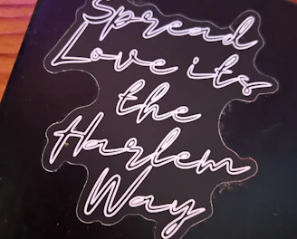A black background with neon-style cursive text that reads 'Spread Love it's the Harlem Way'. The text is bright and stands out against the darker backdrop.