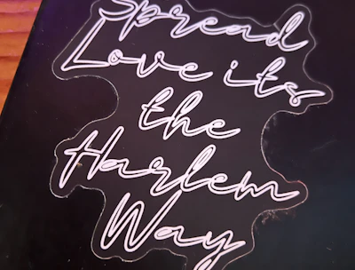 A black background with neon-style cursive text that reads 'Spread Love it's the Harlem Way'. The text is bright and stands out against the darker backdrop.