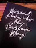 A black background with neon-style cursive text that reads 'Spread Love it's the Harlem Way'. The text is bright and stands out against the darker backdrop.